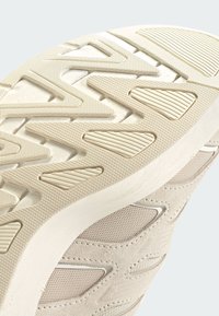 Närbild av en beige sneakersula med texturerade zigzag- och randmönster samt en del av det mesh- och mockaliknande ovandelen.