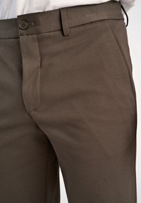 Bruine broek van gladde stof, met een knoopsluiting, platte zakken en een getailleerde pasvorm. Eenvoudig, modern ontwerp.