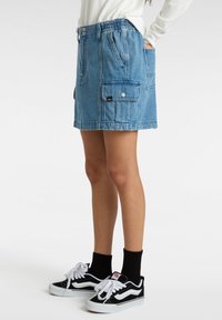 Sininen farkkuhame, jossa on joustava vyötärö, sivutaskut ja applikaatiotasku. Yhdistetty mustiin lenkkareihin ja sukkiin.