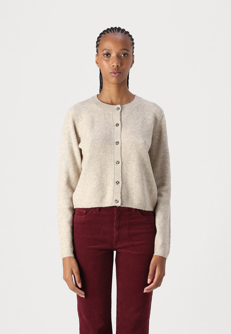 Beige strikket cardigan med rund hals, knappestengning og ribbestrikket kant, sammen med burgunder kordfløyelsbukser med frontlommer.