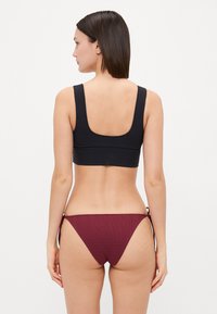 Black crop top with wide straps and a low back paired with maroon ribbed bikini bottoms featuring adjustable ties on the sides.
