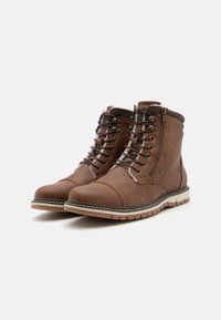 Botas de cuero marrón hasta el tobillo con puntera redonda, cordones en la parte frontal, cremallera lateral y costuras blancas en la suela. Presentan un cuello texturizado y acolchado.