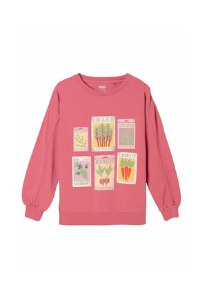 Kvinde med langt mørkt hår, der kigger ned, iført en pink langærmet top og blå jeans, vist bagfra mod en hvid baggrund.