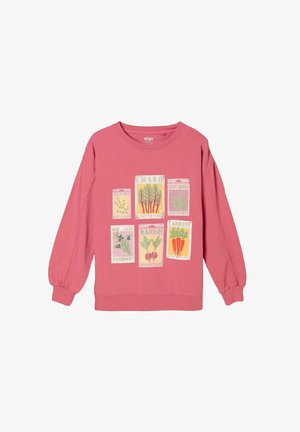 Kvinde med langt mørkt hår, der kigger ned, iført en pink langærmet top og blå jeans, vist bagfra mod en hvid baggrund.