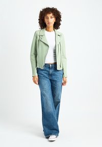 Miętowa zielona skórzana kurtka motocyklowa z zamkami błyskawicznymi, zestawiona z szerokimi, niebieskimi dżinsami o kroju szerokich nogawek i białymi tenisówkami. Prosty top pod kurtką.