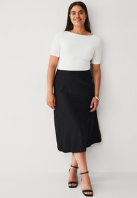Witte fitted top met korte mouwen, gecombineerd met een zwarte midi rok. Zwarte hakken maken de outfit compleet. Eenvoudig ontwerp zonder patronen.