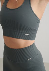 Sujeción deportiva gris con líneas y leggings de cintura alta con acentos metálicos del logo. Tela suave con textura sutil, diseñada para ropa deportiva.