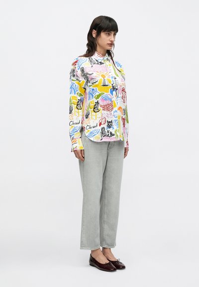 Chemise à manches longues boutonnée blanche, ornée d'un imprimé abstrait coloré. Associée à un jean gris clair coupe droite et des chaussures foncées vernies.