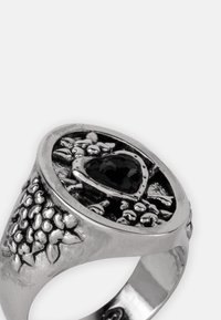 Zilveren ring met een hartvormige zwarte steen, gedetailleerd met sierlijke elementen die op bladeren en takken lijken. Gebogen bandontwerp.