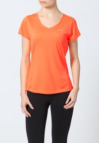 Orange atletisk t-shirt med korta ärmar, v-ringning och diskret logotypdetalj. Slätt, lätt tyg med en figurnära silhuett.