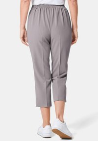 Graue, cropped Hosen mit elastischem Bund und gefaltetem Design. Sie haben eine glatte Textur und werden mit weißen Sneakern kombiniert.