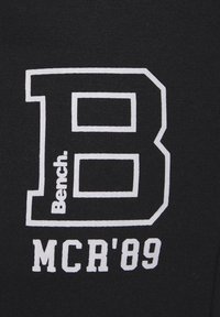 Grande lettre "B" blanche en contour avec le mot "Bench." à l'intérieur et le texte blanc "MCR'89" en dessous sur un fond en tissu noir.