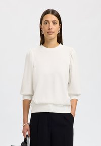 Weißer Pullover mit kurzen, gepufften Ärmeln, rundem Ausschnitt und lockerer Passform. Glatte Textur, einfarbig, kombiniert mit dunklen Hosen.