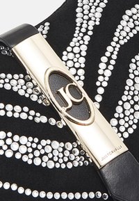 Musta mokkanahkainen käsilaukku, jossa on hopeisia strassikiviä aaltoilevassa kuviössä. Varustettu kullanvärisellä soljella, jossa on "JC"-logo.