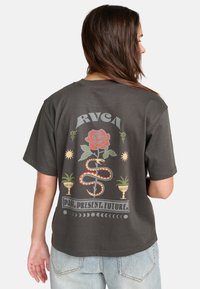Čierny bavlnený T-shirt s grafickým potlačou na chrbte: ruža, had a text "MINULOSŤ. PRÍTOMNOSŤ. BUDÚCNOSŤ." vytlačené v farebných dizajnoch. Voľný strih, krátke rukávy.