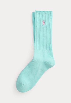Para jasnoniebieskich skarpetek za kostkę z prążkowanego materiału, z małym różowym haftowanym logo po boku, ułożonych na płasko na białym tle.