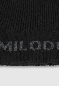Black ribbed knit fabric featuring a textured pattern and a faded gray logo. The texture appears soft and slightly fuzzy.