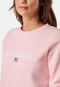Felpa rosa con collo rotondo, morbida al tatto e grafica frontale con testo tra cui "SEASIDE" e un dettaglio della bandiera americana.