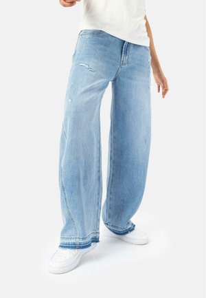 Light blue wide-leg jeans with distressed details and frayed hems, paired with white sneakers on a plain background.