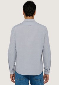 Camicia azzurra a maniche lunghe con colletto classico, polsini con bottone e orlo arrotondato. Realizzata in un tessuto liscio con una sottile texture.