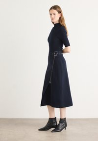 Robe marine en tissu côtelé, avec un col montant, des manches courtes, un corsage ajusté, une taille ceinturée et un détail de fermeture éclair sur le côté.
