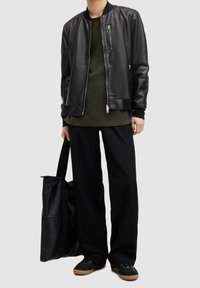 Svart läderbombarjacka, grön stickad skjorta, vida svarta byxor och svart väska. Skor med bruna sulor och svarta snören.