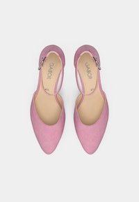 Ροζ σουέντ γόβες με ψηλό τακούνι, μυτερή μύτη και λουράκι στον αστράγαλο με ασημί πόρπη. Το εσωτερικό είναι μπεζ με το λογότυπο της μάρκας.