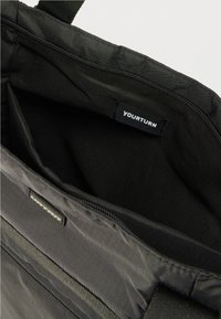 Μαύρη τσάντα ώμου με φερμουάρ, εσωτερικά διαθέτει απλή μαύρη επένδυση. Η ετικέτα γράφει «YOURTURN». Υφασμάτινη υφή με λείο φινίρισμα.