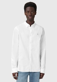 Camicia bianca a maniche lunghe con colletto button-down, dotata di un piccolo logo argento sul petto e una superficie in cotone liscia.