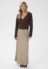 Barna textúrájú, hosszú ujjú felső, amelyet egy légies bézs maxi szoknyával és szőtt barna cipővel párosítottak. Egyszerű, puha anyagból készült dizájn.