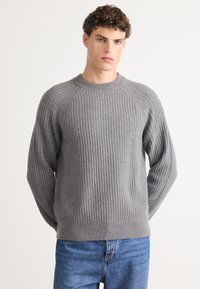 Gray ribbed sweater with a crew neckline and raglan sleeves, made from textured fabric; paired with blue jeans.