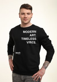 Felpa nera con testo bianco "ARTE MODERNA. VIBRAZIONI SENZATEMPO." e logo "apoh London". Collo a giro, maniche lunghe e polsini a costine.