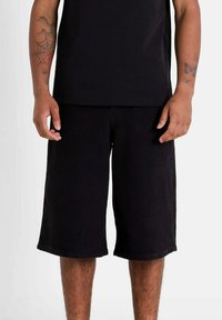 Pantalones cortos de algodón negros con un ajuste relajado, hasta la rodilla, de color sólido y sin patrones o adornos visibles.