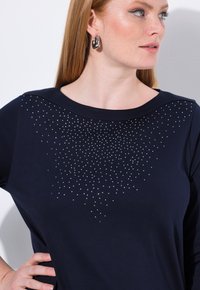 Maglietta a maniche lunghe blu navy con scollatura rotonda e una gradazione di strass argentati sul petto, realizzata in un tessuto morbido e liscio.