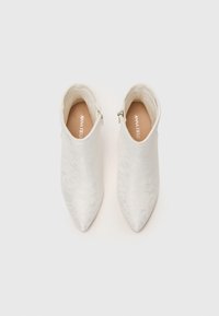 Paire de bottines blanches à bout pointu avec fermetures éclair latérales et motif texturé subtil sur un fond clair.