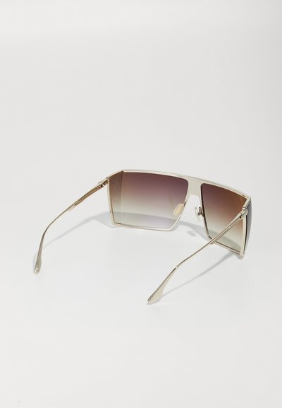 Lunettes de soleil avec de grandes montures carrées, finition métallique dorée et verres dégradés marron. Fines branches avec des détails subtils.