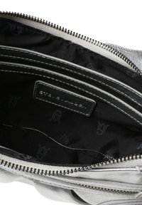 Interior de un bolso de cuero sintético plateado con un forro negro, que cuenta con un bolsillo con cremallera y una etiqueta con "STEVE MADDEN" grabada en ella.
