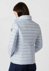 Chaqueta acolchada azul claro con textura acanalada, cuello alto y parche con logo en el hombro. Cuenta con bolsillos delanteros y diseño ajustado.