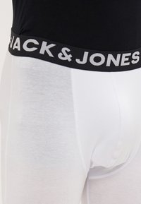 Hvite bomullsbokser med svart elastisk midjebånd som har "JACK & JONES" skrevet i hvit skrift. Glatt tekstur og tettsittende design.