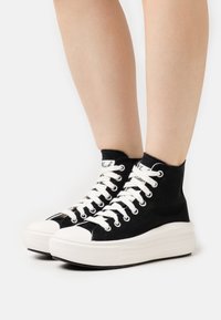 Czarne sneakersy za kostkę z białymi sznurowadłami, tekstylnym cholewką i platformą, z zaokrąglonym noskiem i kontrastowym przeszyciem.