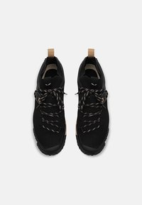 Sorte atletiske sko med overdel i mesh, teksturerte svarte såler og brune detaljer. Har svarte og grå mønstrede snører og draremmer.
