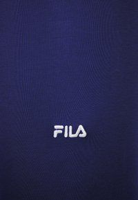 Logo de FILA bordado en blanco sobre un fondo de tela azul oscuro.