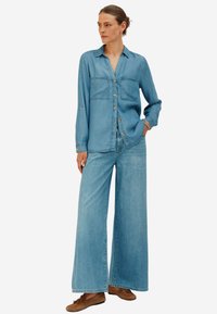 Camicia di jeans azzurro chiaro con chiusura a bottoni, due tasche sul petto e pantaloni in denim a gamba larga, tutti in una tonalità coordinata di azzurro chiaro.