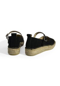 Schwarze Wildleder-Espadrilles mit einer gewebten Jutesohle, ausgestattet mit einem Schnallenriemen und einem offenen Fersen-Design. Strukturierte Oberseite und natürliche Sohle.