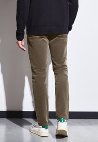 Beżowe spodnie z korduroju o dopasowanym kroju, w zestawieniu z białymi sneakersami z zielonymi akcentami. Widok pokazuje tył stylizacji.