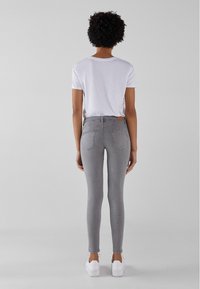 Jeans ajustados grises con una cintura de altura media, que cuentan con bolsillos traseros y una textura suave, combinados con una camiseta blanca y zapatillas blancas.