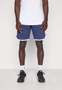 Calções atléticos azul-marinho com detalhes brancos, feitos de tecido suave. O modelo veste uma t-shirt branca, ténis pretos e meias brancas.