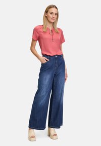 Korallfärgad kortärmad topp med dragsko-detalj, kombinerad med vida blå denimjeans och beiga plattformsskor med sidofickor.