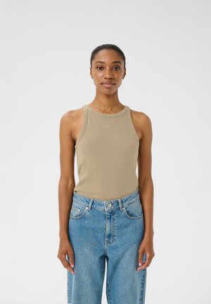 Beige ribbed tank top with a round neckline and racerback design. Worn with high-waisted light blue jeans. Simple logo detail at the chest.