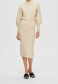 Beige knit top with a high neckline and puff sleeves, paired with a matching fitted midi skirt featuring a side slit, worn with black open-toe shoes.